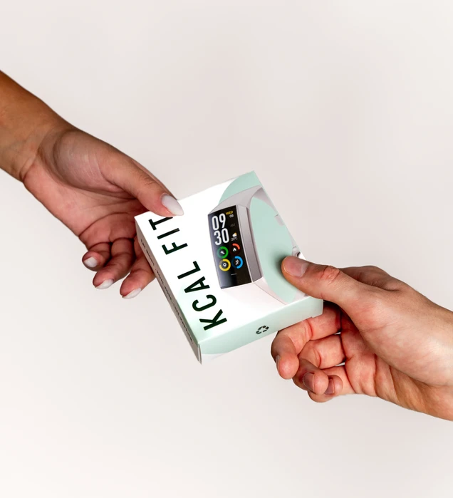 Two hands exchange a boxed smart fitness tracker labeled KCAL FIT, showing its colorful display. The setting is a plain background, emphasizing the handover.