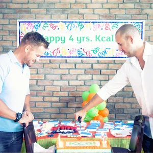 Kcal Founders Andreas L Borgmann and Mark Carroll are celebrating Kcal's 4th anniversary by cutting cake in the office.