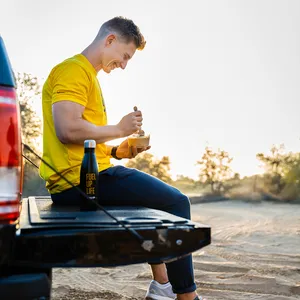 Healthy-looking man with a yellow Fuel-Up t-shirt sitting on the back of a pickup truck eating nutritious meal-prepped food.