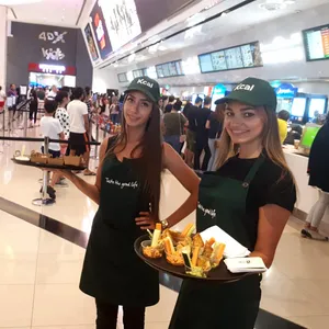 Two women in Kcal hats and aprons handing out healthy snacks outside VOX Cinemas in Dubai.