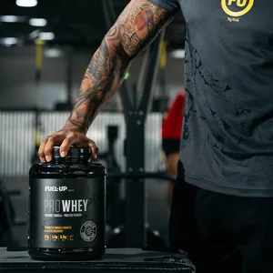 A man dressed in gym wear resting his hand on a Fuel-Up Pro Whey Protein container in the gym.