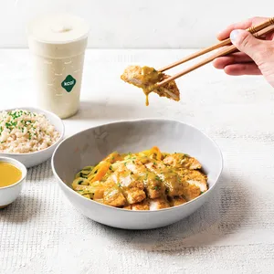 A Kcal Katsu Curry in a white bowl with a hand using chopsticks to pick up a breaded piece of chicken covered in Katsu sauce.