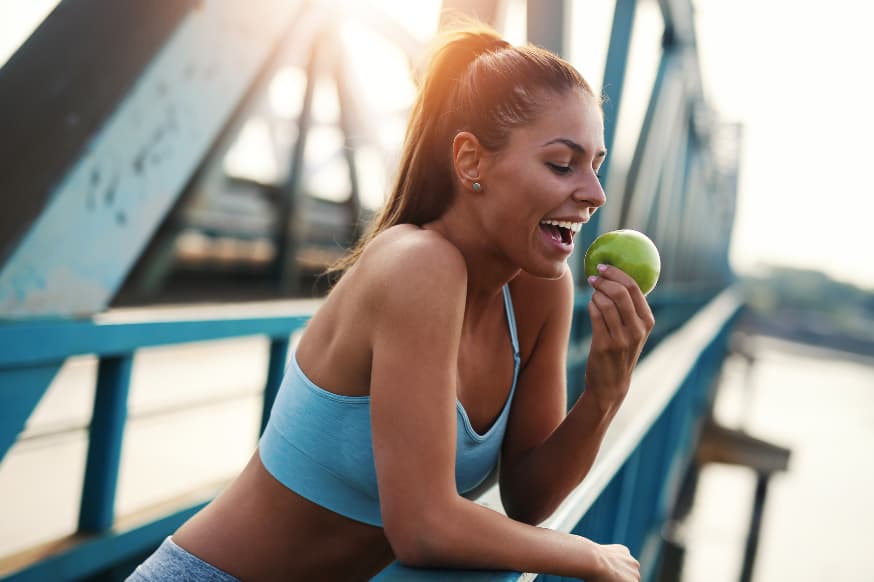 Healthy woman standing on a bridge enjoying the view eating an apple