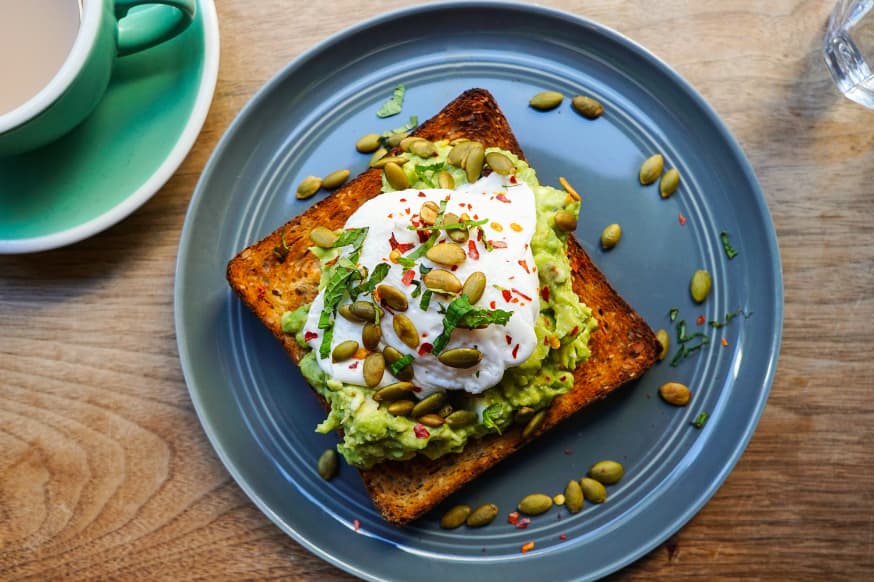 Avocado on square brown toast with poached egg on a blue plate