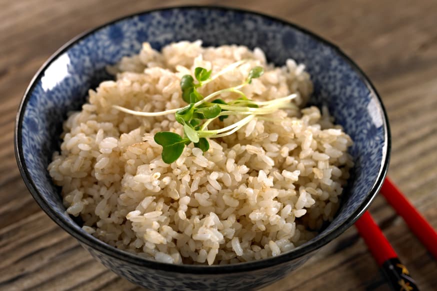 Dark grey bowl of fluffed brown rice on a table with chopsticks