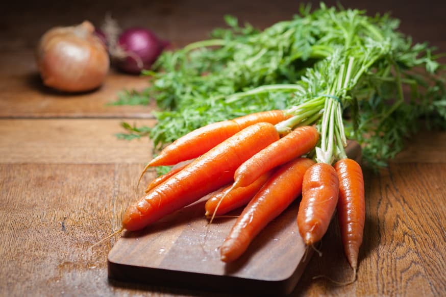 Bunch of raw carrots with the stems on a wooden chopping board with onions