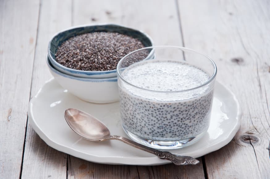 Bowl of raw chia seeds on a plate with a chia seed pudding