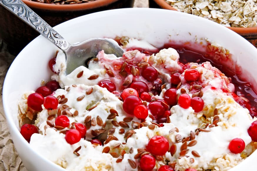 A white bowl of berries, yoghurt, oats and flaxseeds