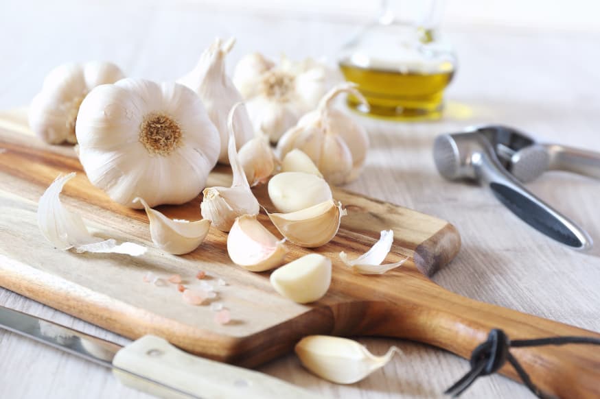 Garlic cloves, unpeeled garlic heads and a garlic press on a chopping board