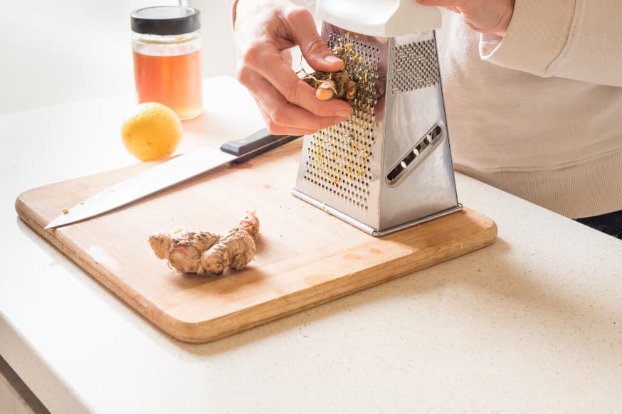 Man grating ginger on a wooden chopping board