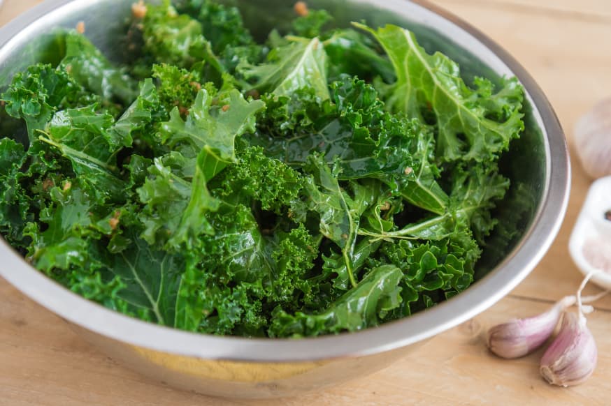 Steel mixing bowl filled with raw kale with two cloves of fresh garlic on the table