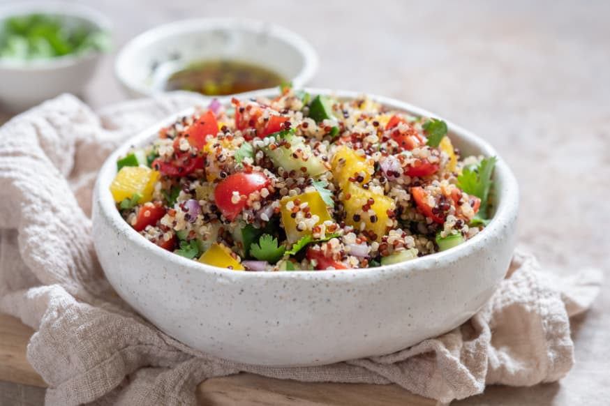 A quinoa mixed salad in a white bowl placed on a cream napkin