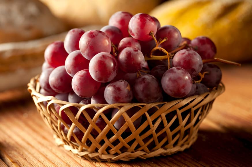 A bunch of stem-on red grapes in a wooden basket