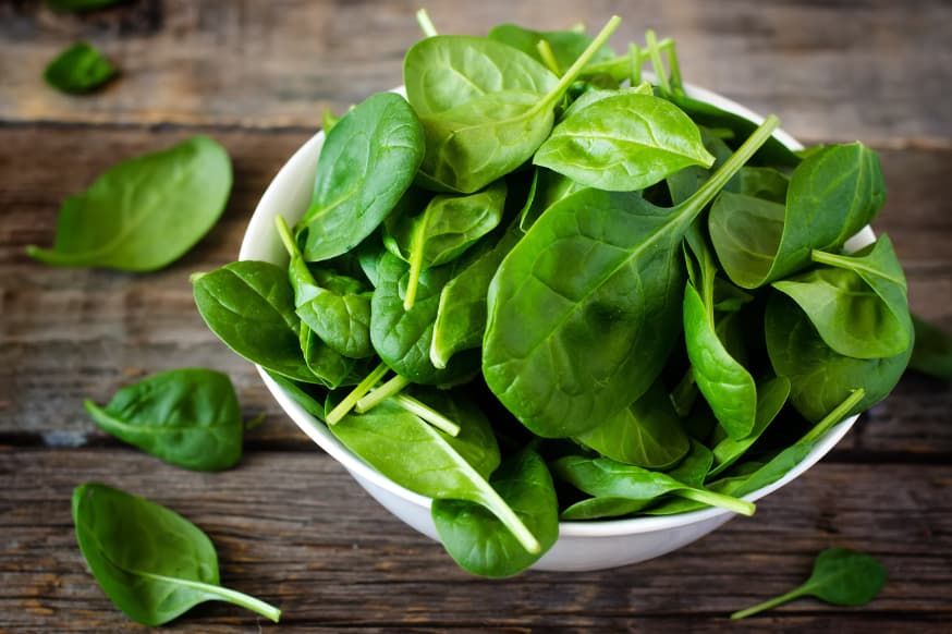 Small white bowl of raw spinach on a wooden work surface