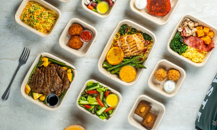 Top view of assorted healthy meals in eco-friendly containers arranged on a marble surface.