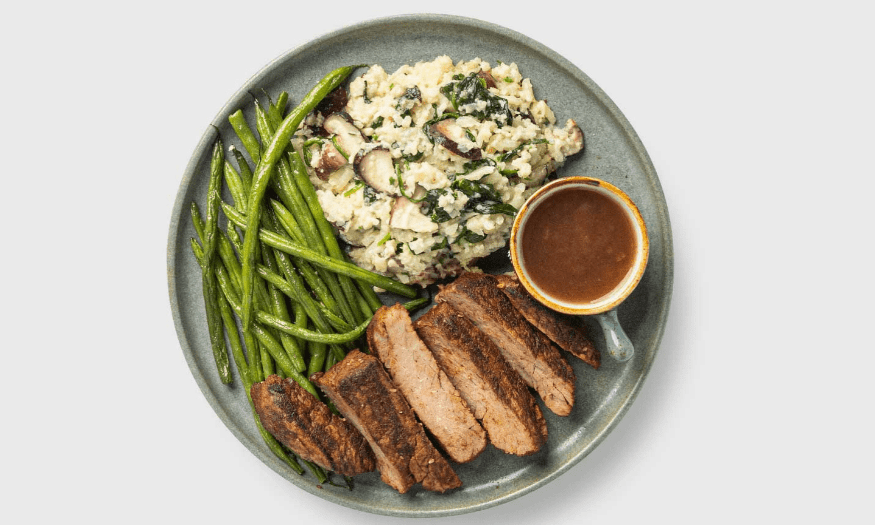 Plate of balanced meal with sliced beef, green beans, vegetable mash, and a side of gravy.