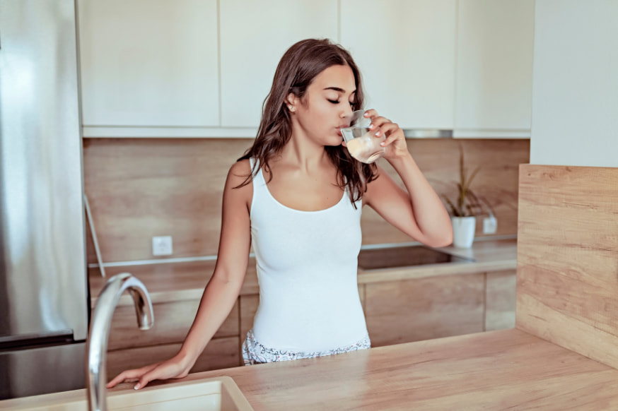 Woman drinking water in the kitchen first thing in the morning. 