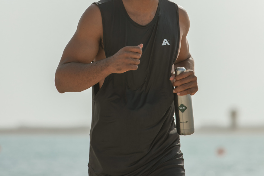 Man going for a morning job on the beach holding a Kcal thermos bottle. 