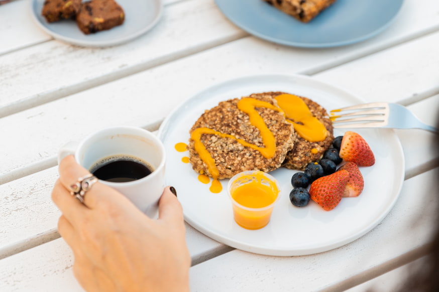 Kcal healthy breakfast pancakes and a cup of coffee on a white wooden table. 
